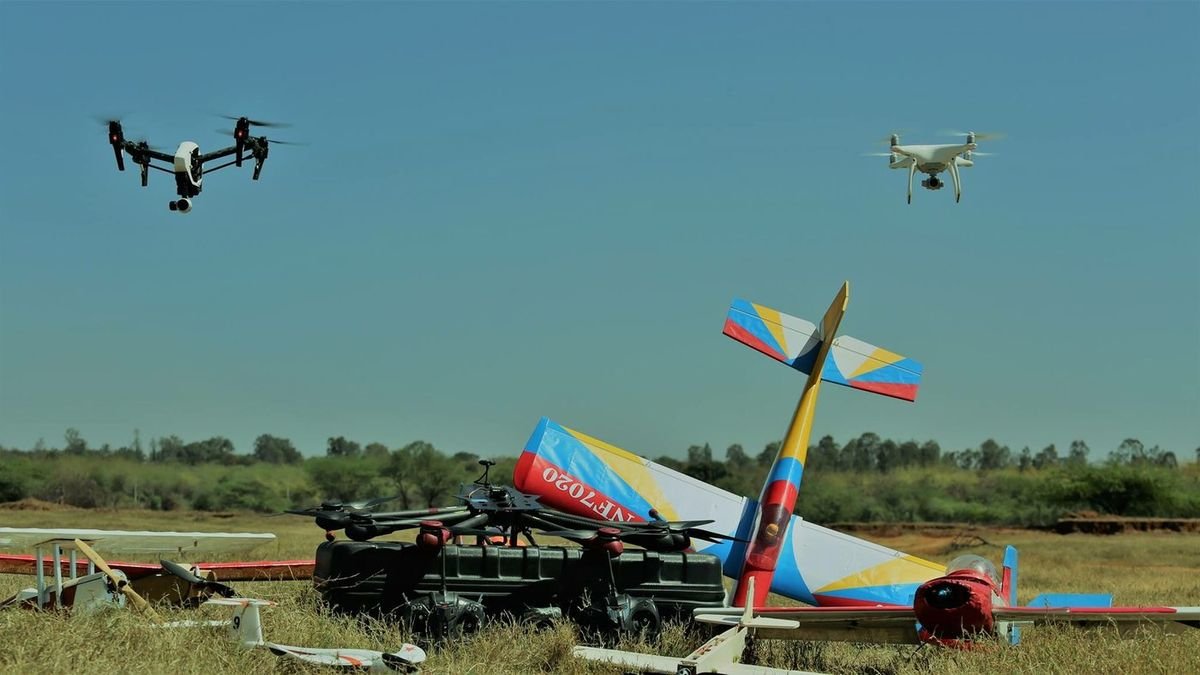 Multirotor aircraft airborne over a field flight line with ground equipment and cases laid out