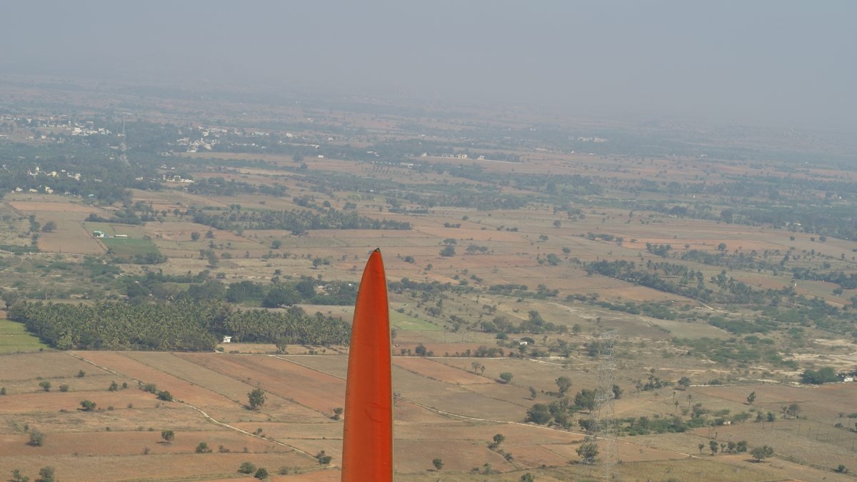 Wind turbine blade tip photographed from a drone against farmland below